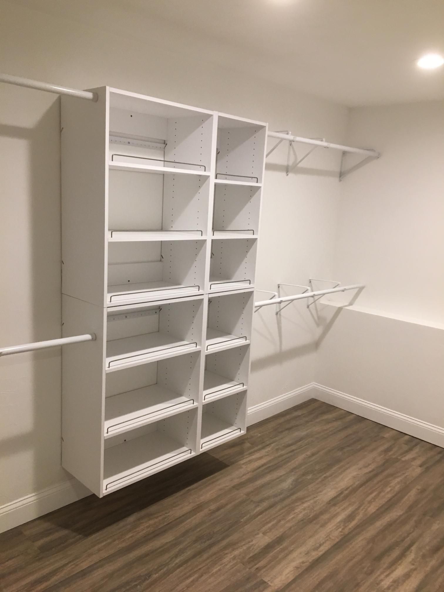 White closet organizer with shelves and hanging rods in a room with wood-look flooring and white walls.