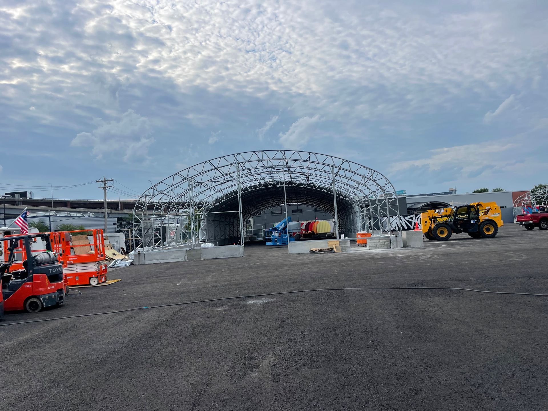 Construction site with large metal frame structure and heavy machinery on asphalt.