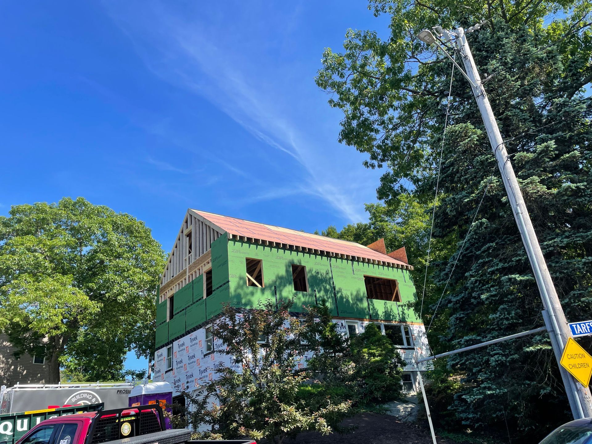 Building under construction with green siding, surrounded by trees under a blue sky.
