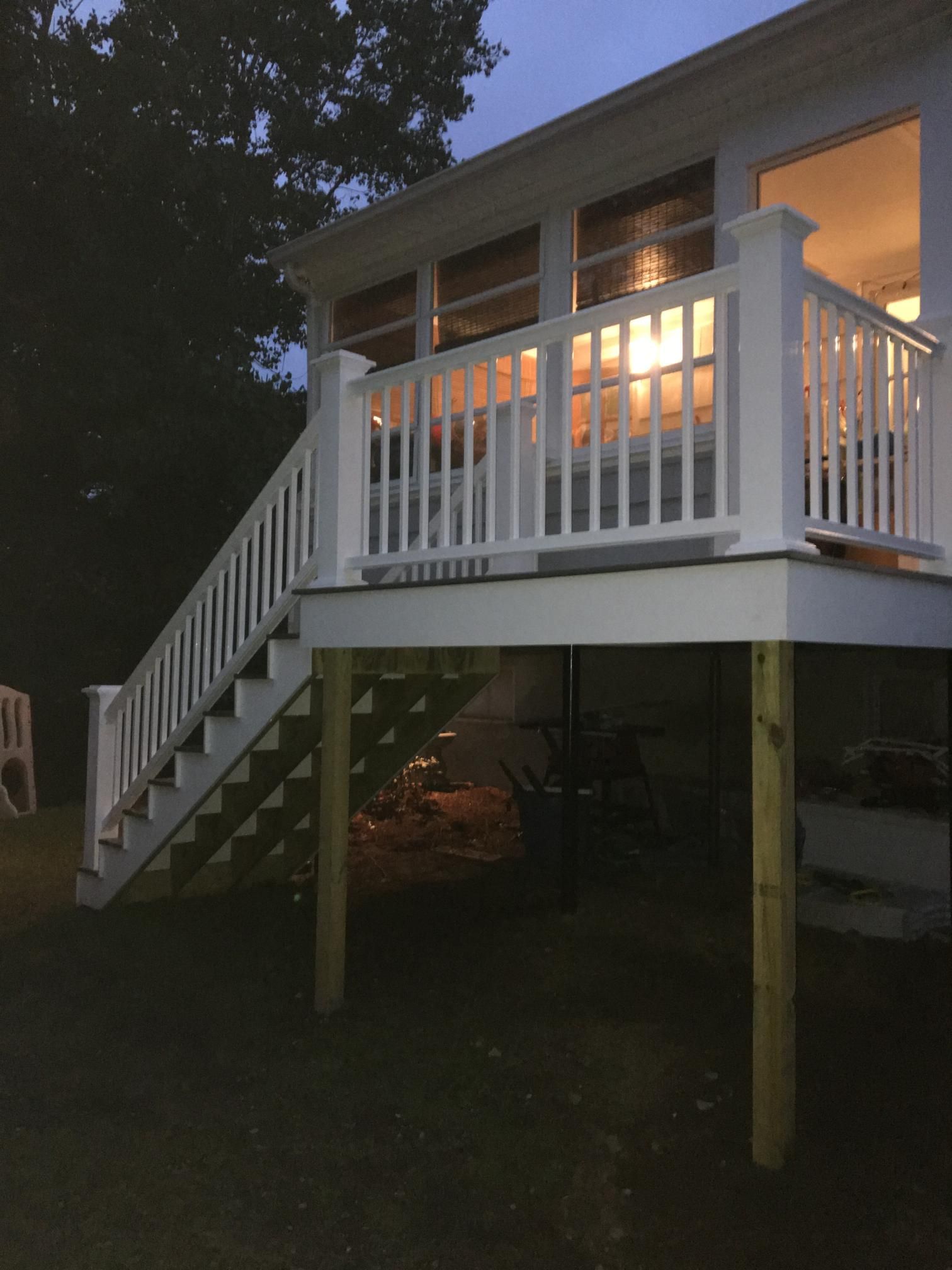 White deck with stairs attached to a house, lit from inside. Outdoors at dusk.