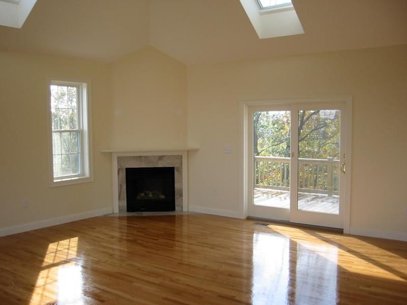 Empty room with fireplace, window, and glass doors; hardwood floor, sunlight.