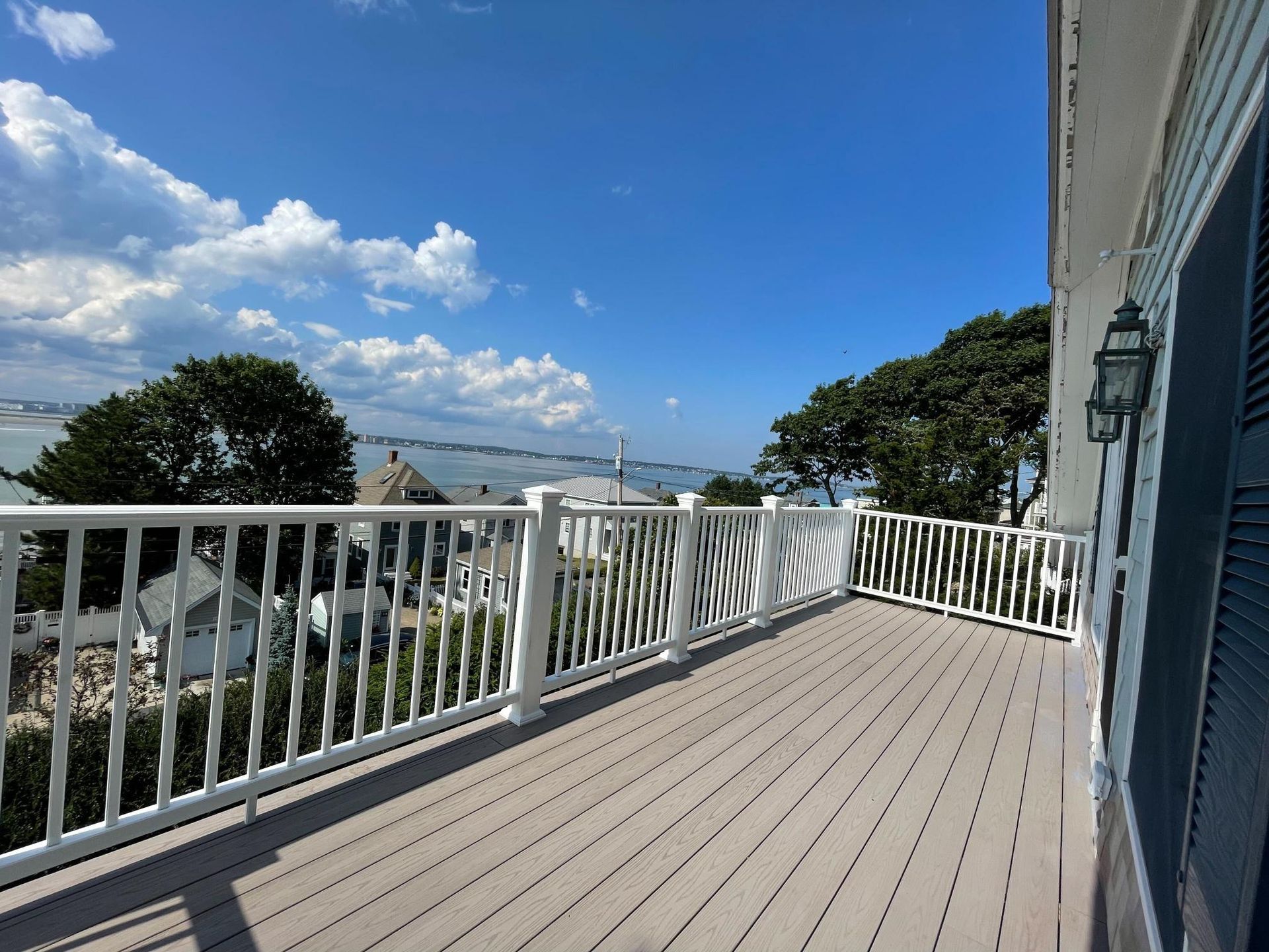 Spacious outdoor deck with white railing overlooking a coastal town and blue sky.
