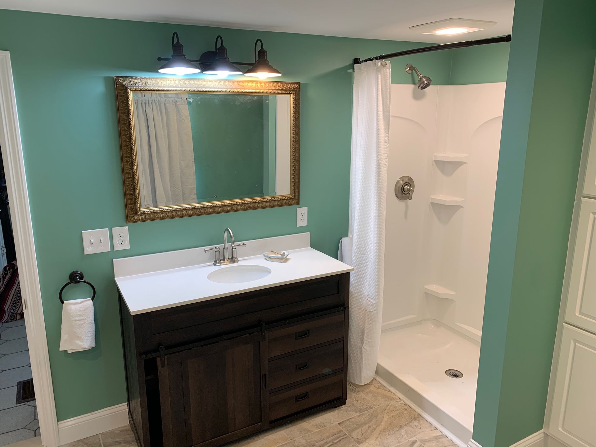 Bathroom with teal walls, dark vanity, white countertop, and shower.