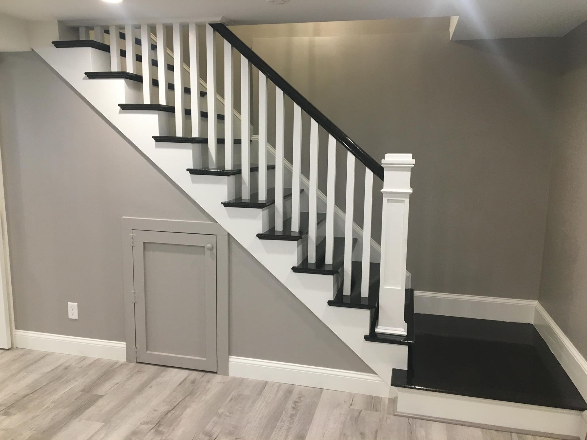 Staircase with black treads, white risers, and railing, in a room with gray walls and light wood flooring.