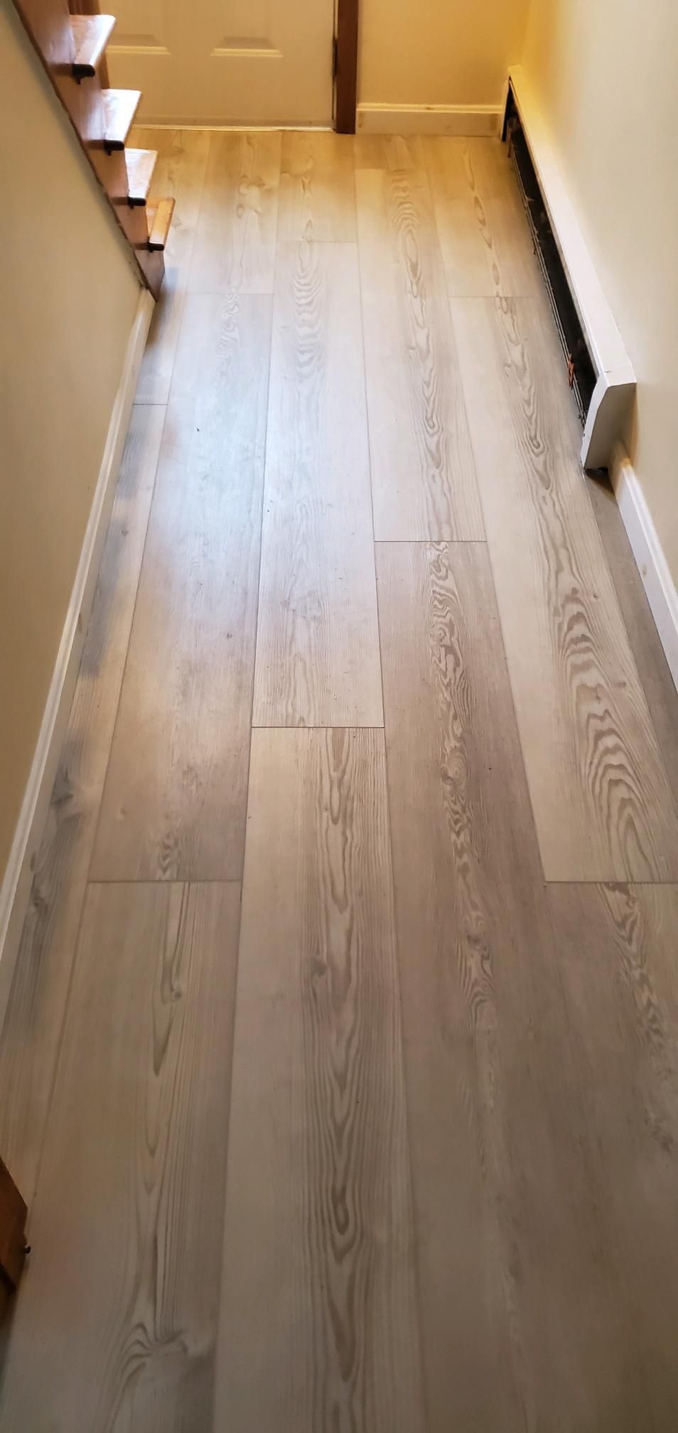 Wooden plank flooring in a hallway with stairs on the left and a white radiator on the right.