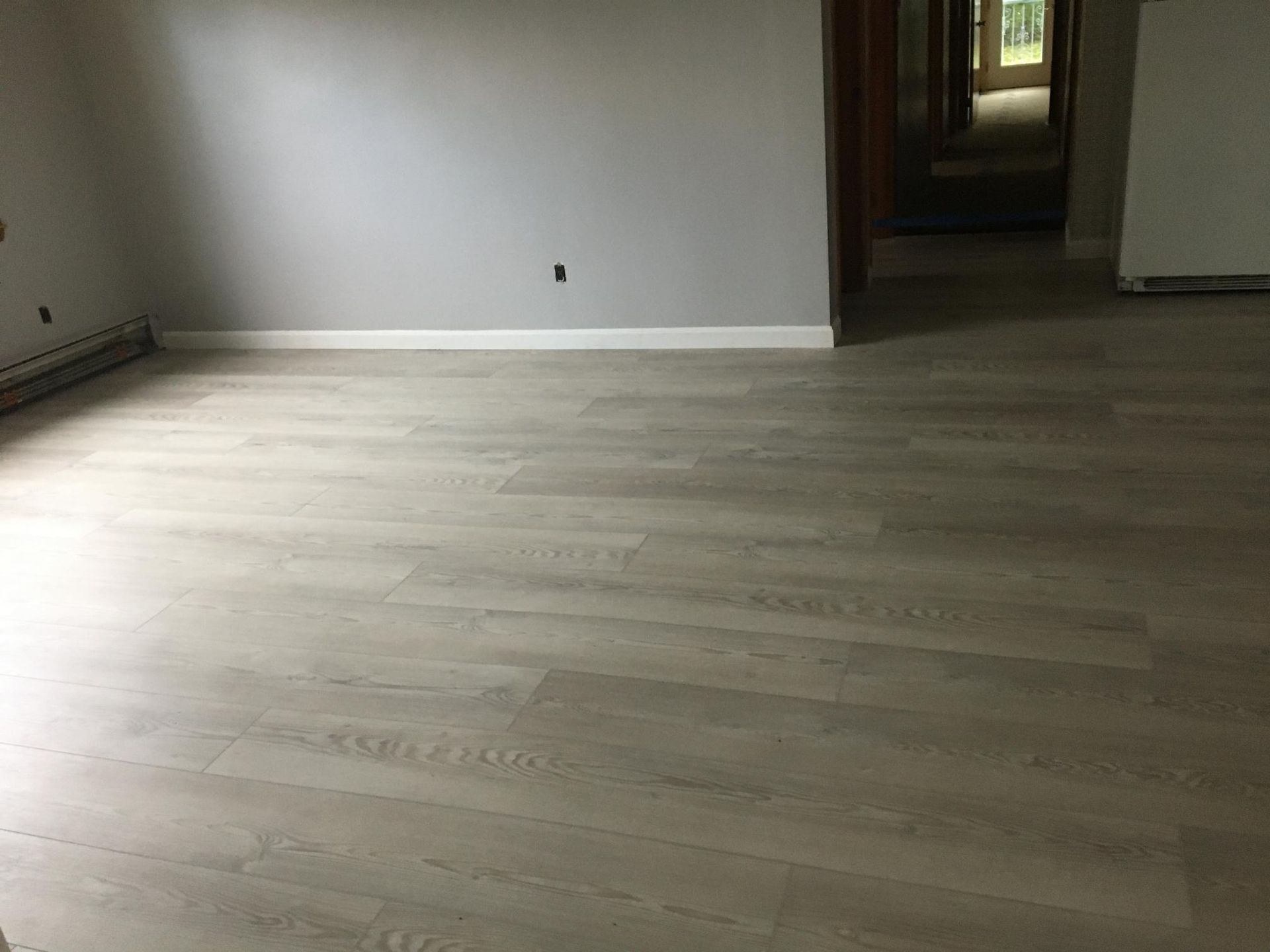 Empty room with light wood-look flooring, gray walls, and white baseboards.