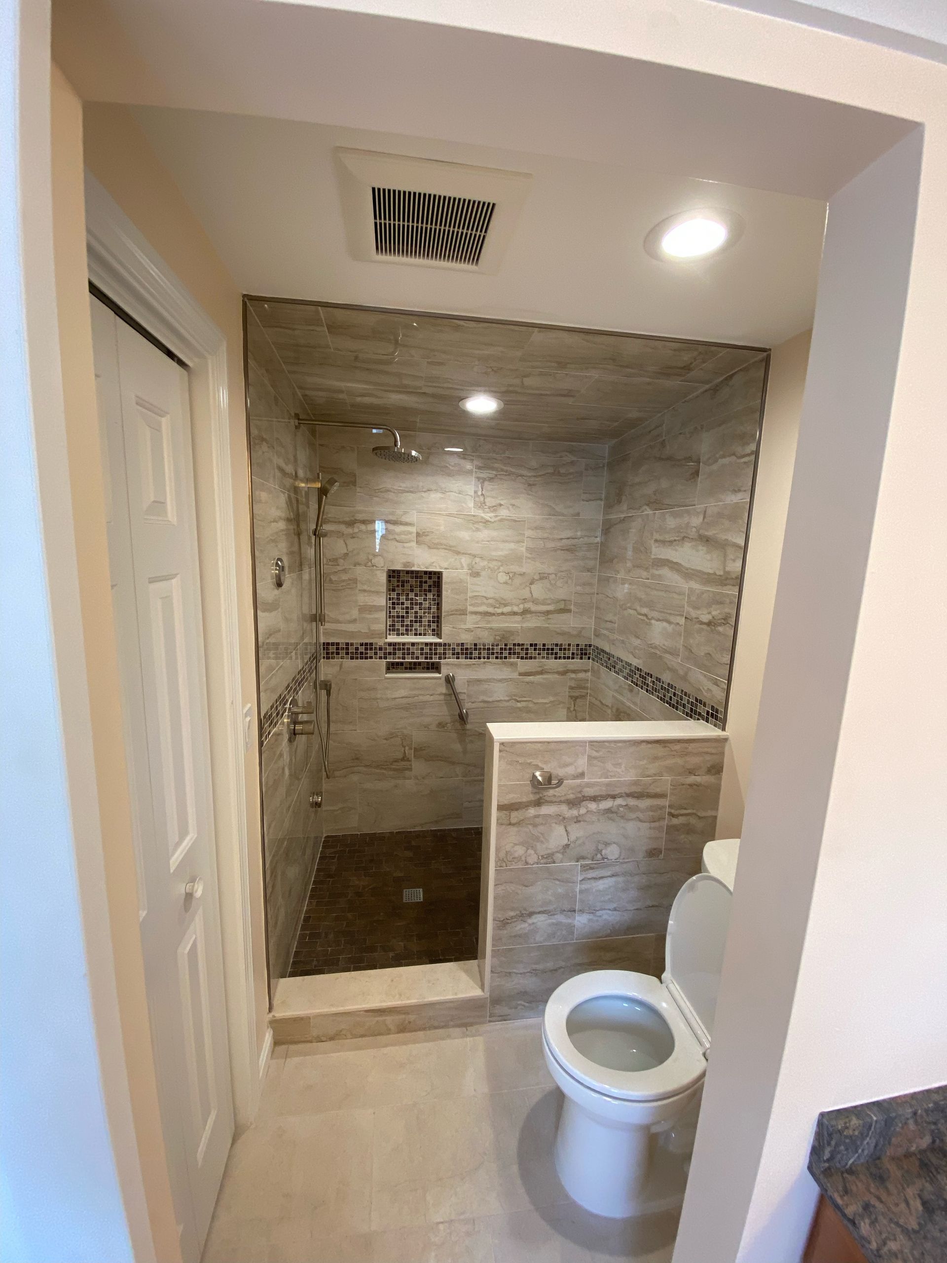 Bathroom with tile shower, toilet, and a partially open door. Beige and grey tones.