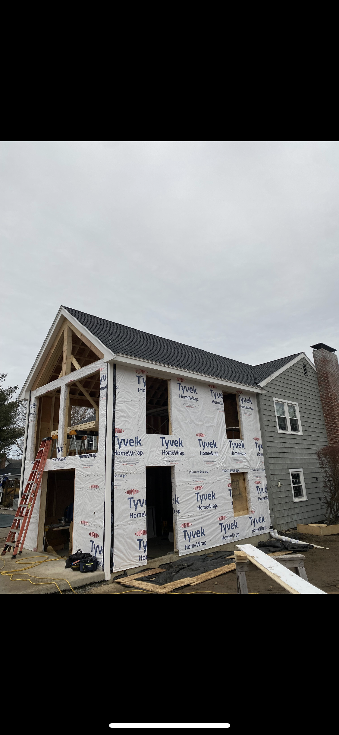 House under construction, with new structure attached to an existing building, surrounded by scaffolding and wrapped in white Tyvek.