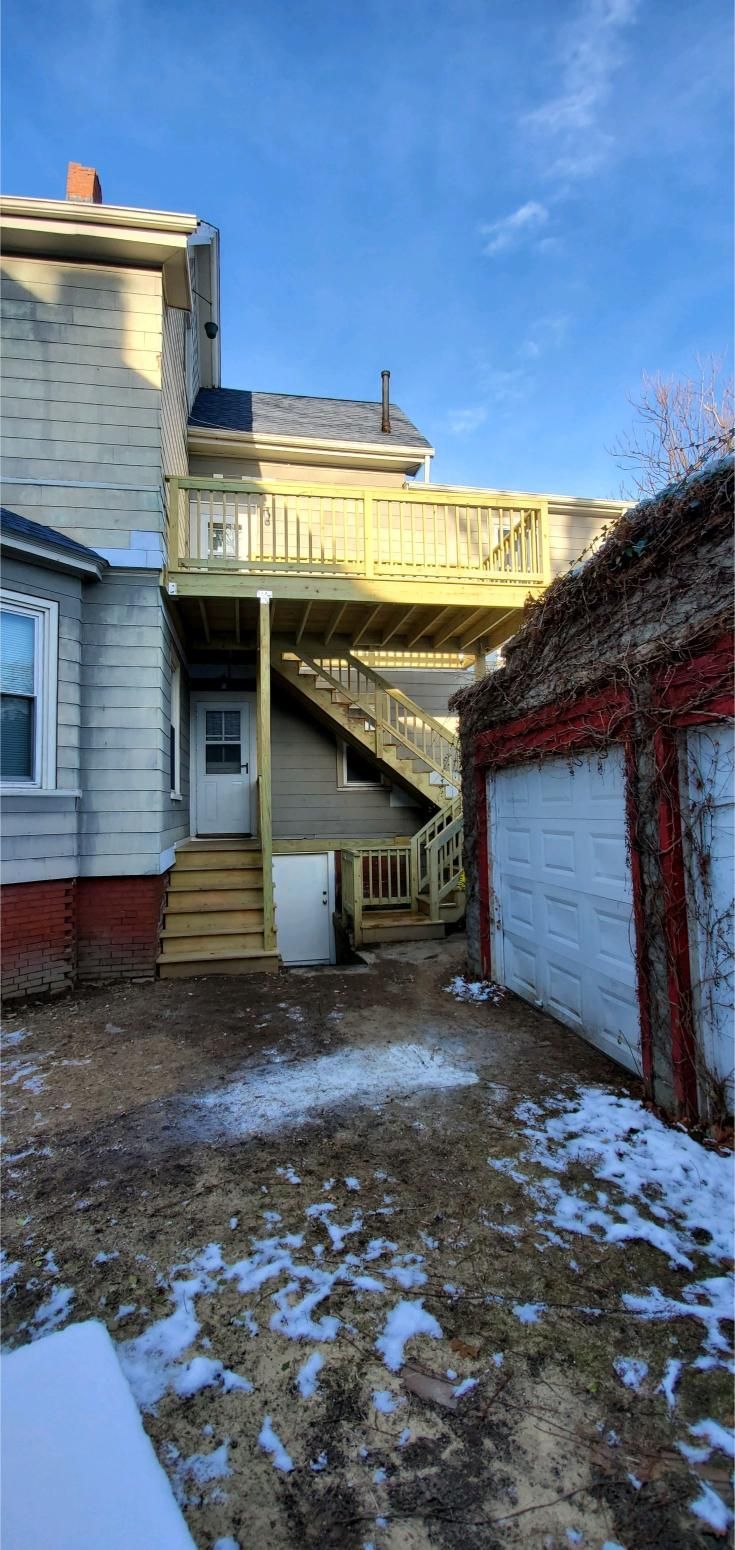 Backyard view with a wooden deck, stairs, and a garage under a blue sky.