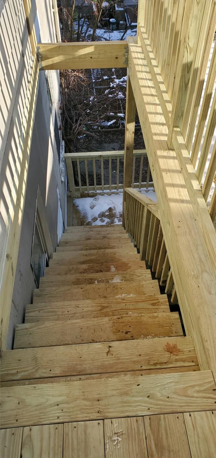 Wooden outdoor staircase leading down from a deck with snow in the background.