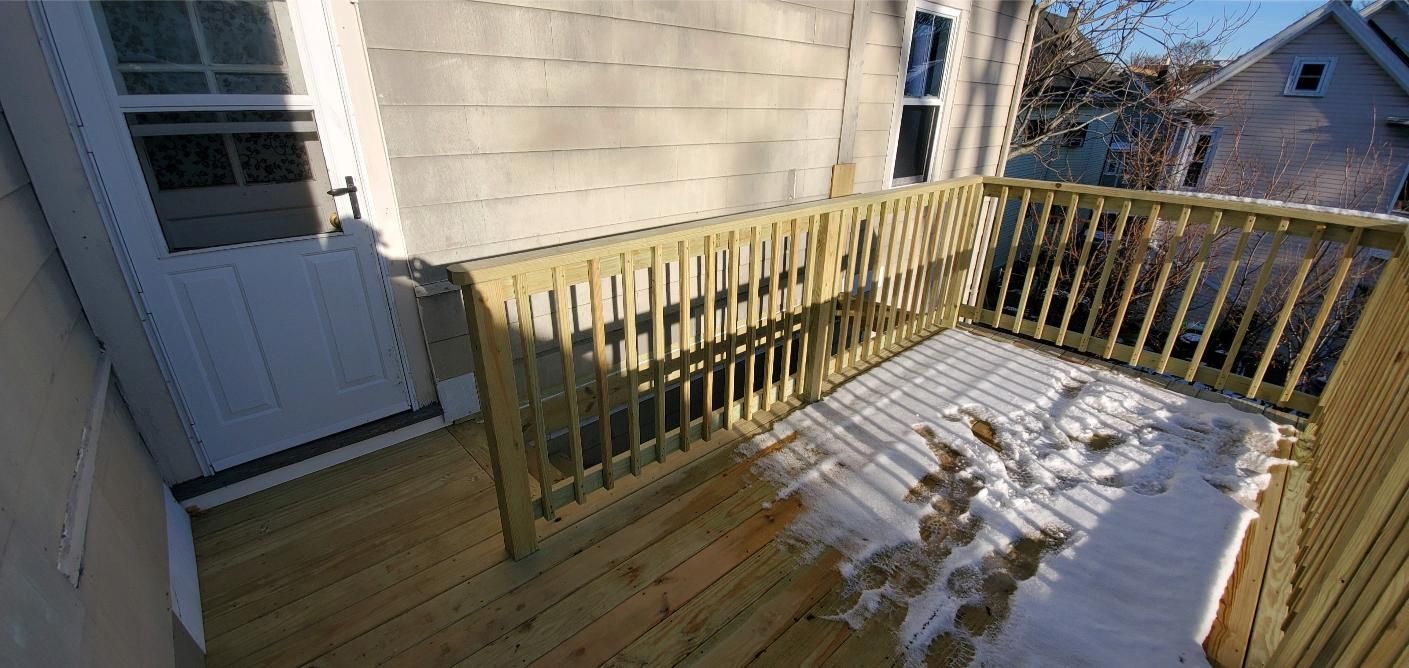 A wooden deck covered in snow, with a railing and a door leading to the house.