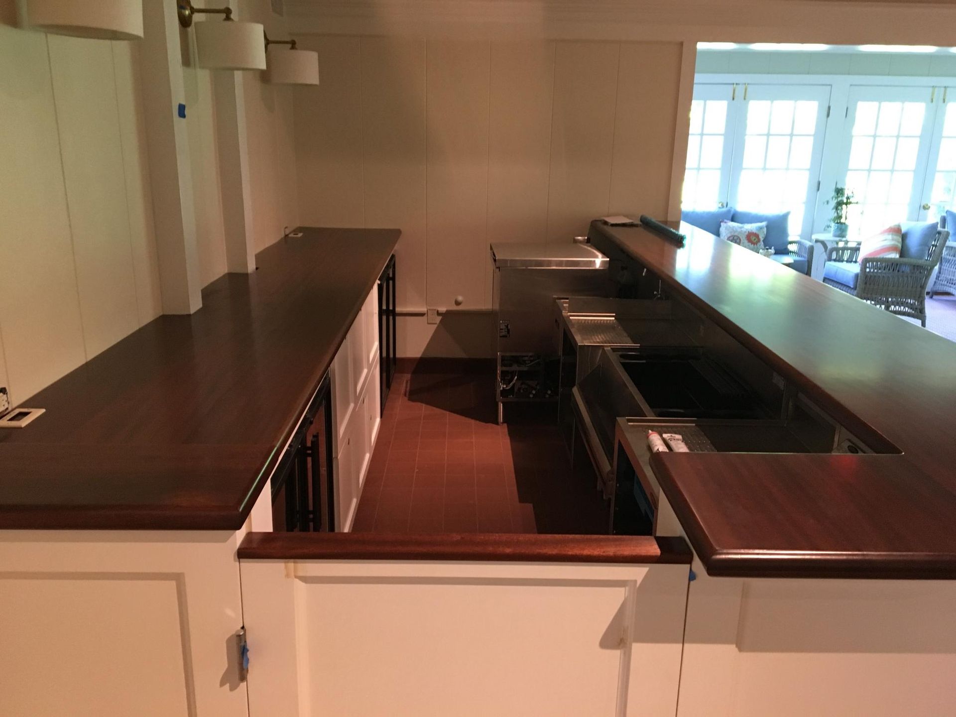 A bar area with a dark wooden counter and stainless steel sinks, surrounded by white walls.