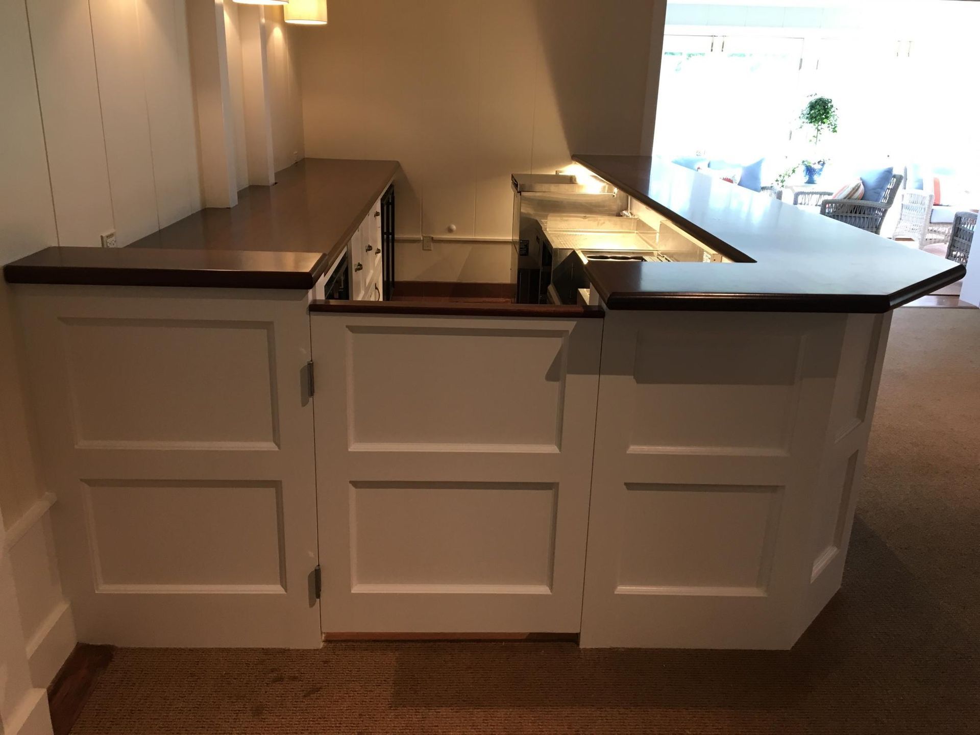White bar with dark wood countertop. The bar has a right angle shape with built-in storage doors.