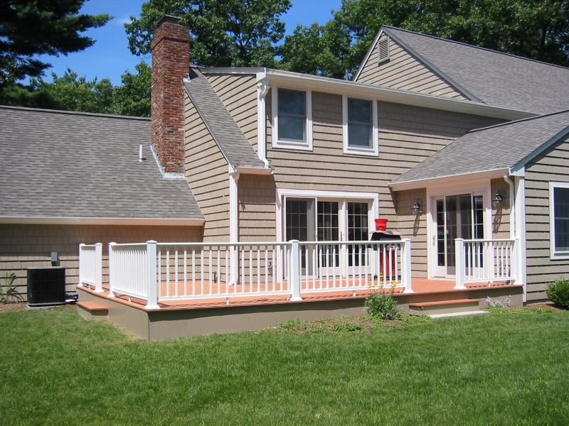 Tan house with white deck and railing; red brick chimney.