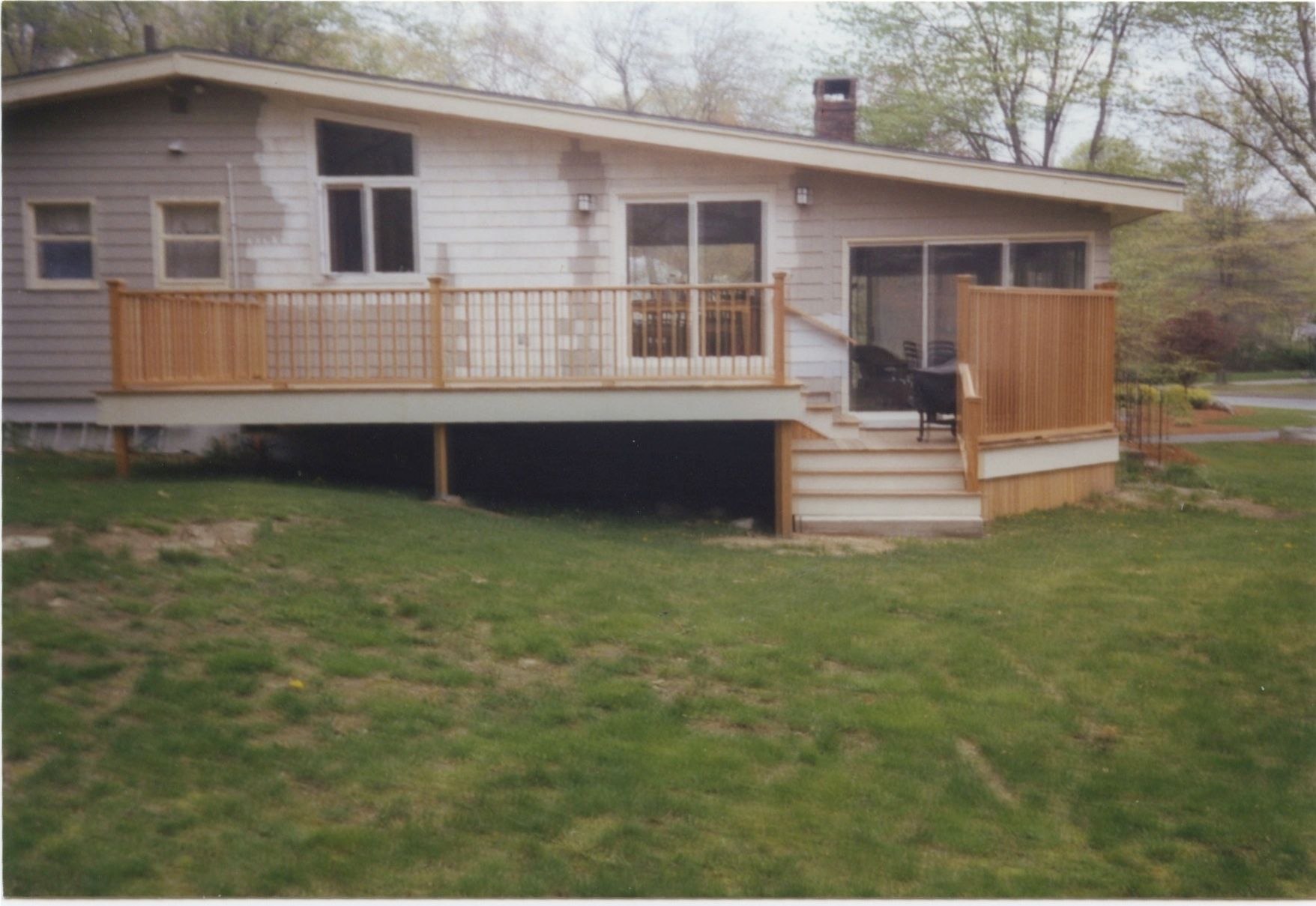House with a wooden deck and stairs leading to a grassy yard; exterior view.