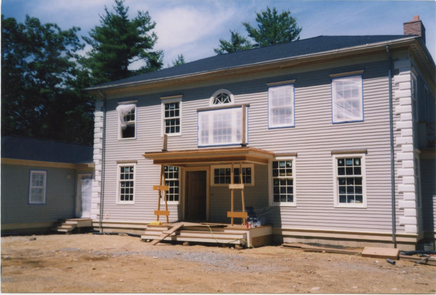 Two-story house with light siding and porch under construction. Windows and door visible.