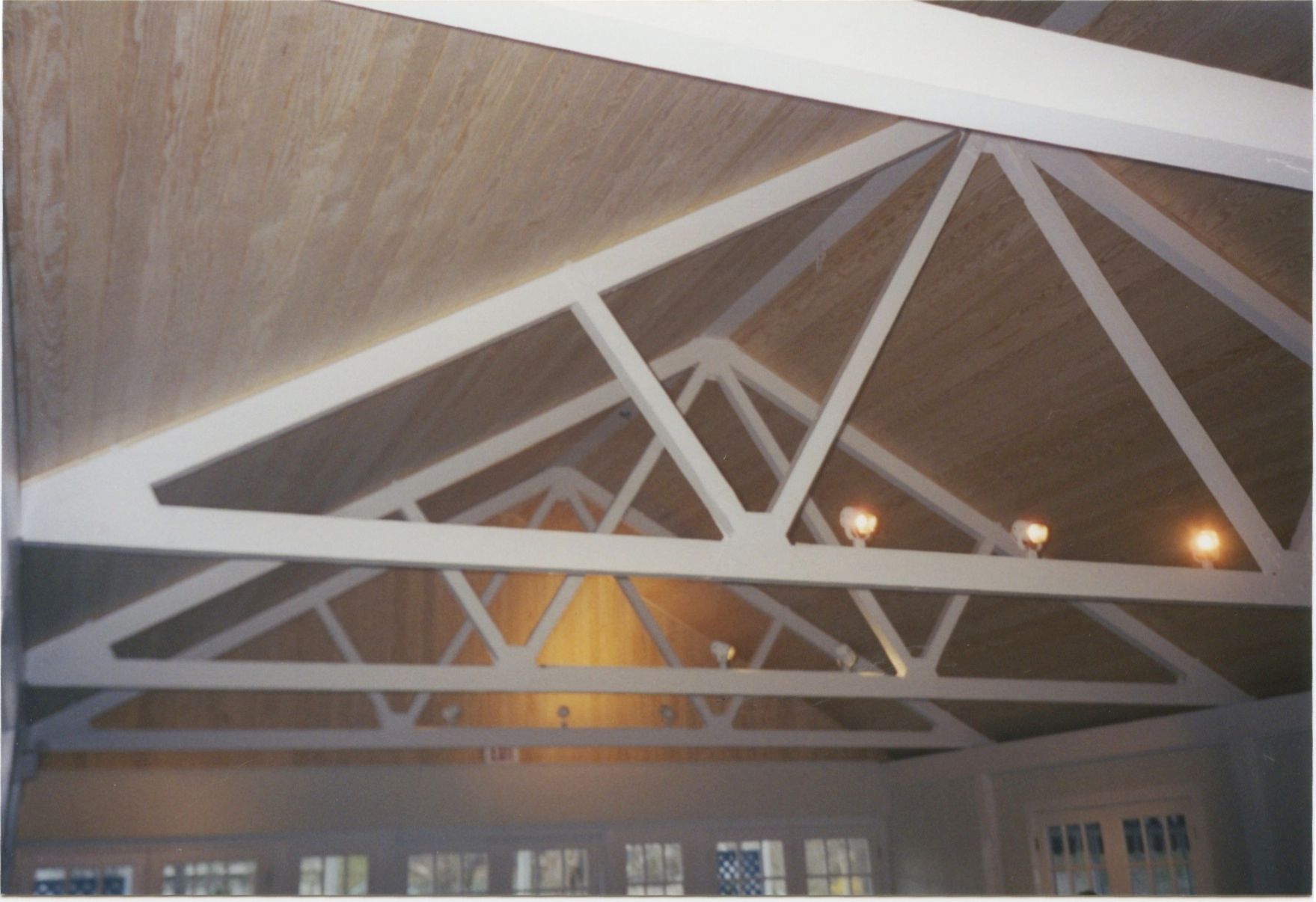 White-painted wooden rafters in a peaked roof with recessed lights. Beige ceiling.