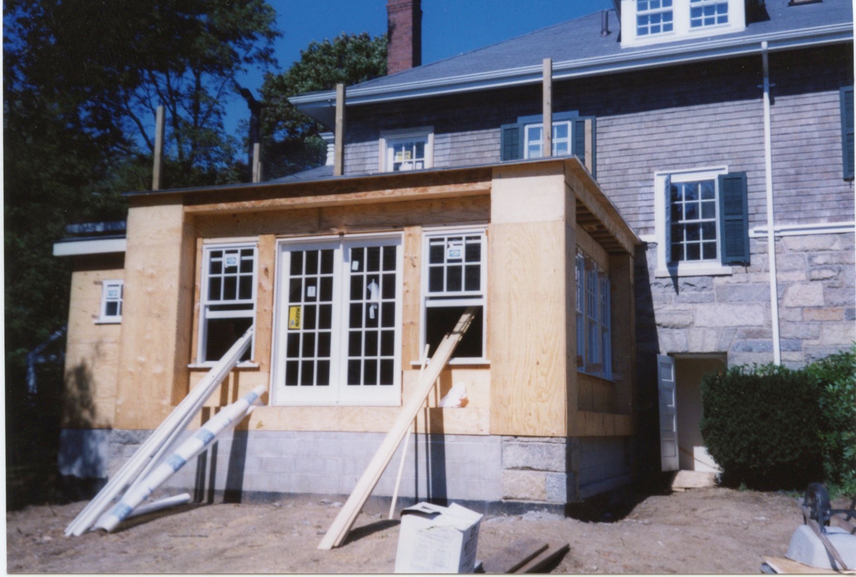 Construction of a room addition to a stone house; framing and windows installed, wood beams support roof.
