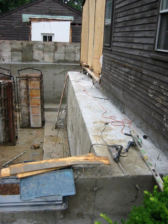 Construction site: concrete retaining wall under construction next to a dark-sided building.