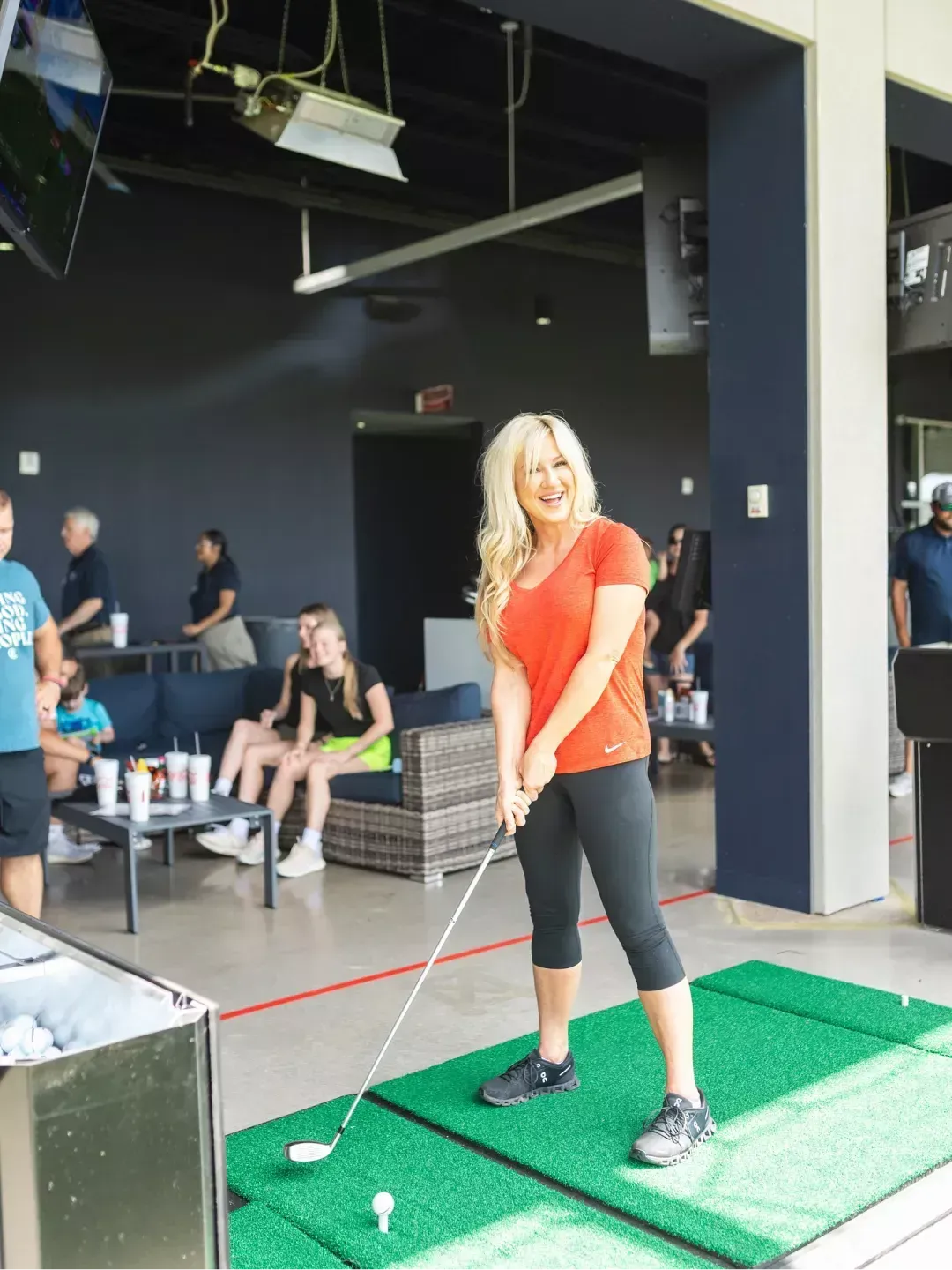 A woman is swinging a golf club on a green mat