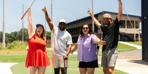 A group of people are standing on a golf course holding golf clubs in the air.