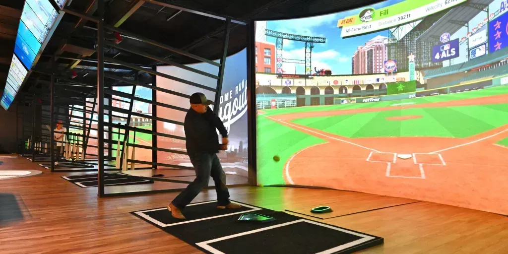 A man is playing a video game on a baseball field.