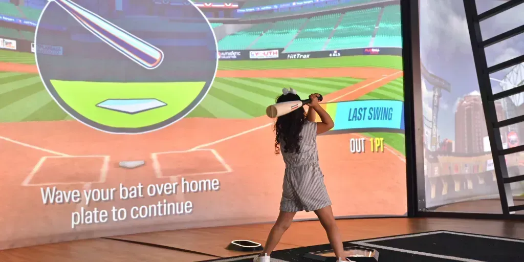 A woman is swinging a baseball bat at a virtual baseball game.