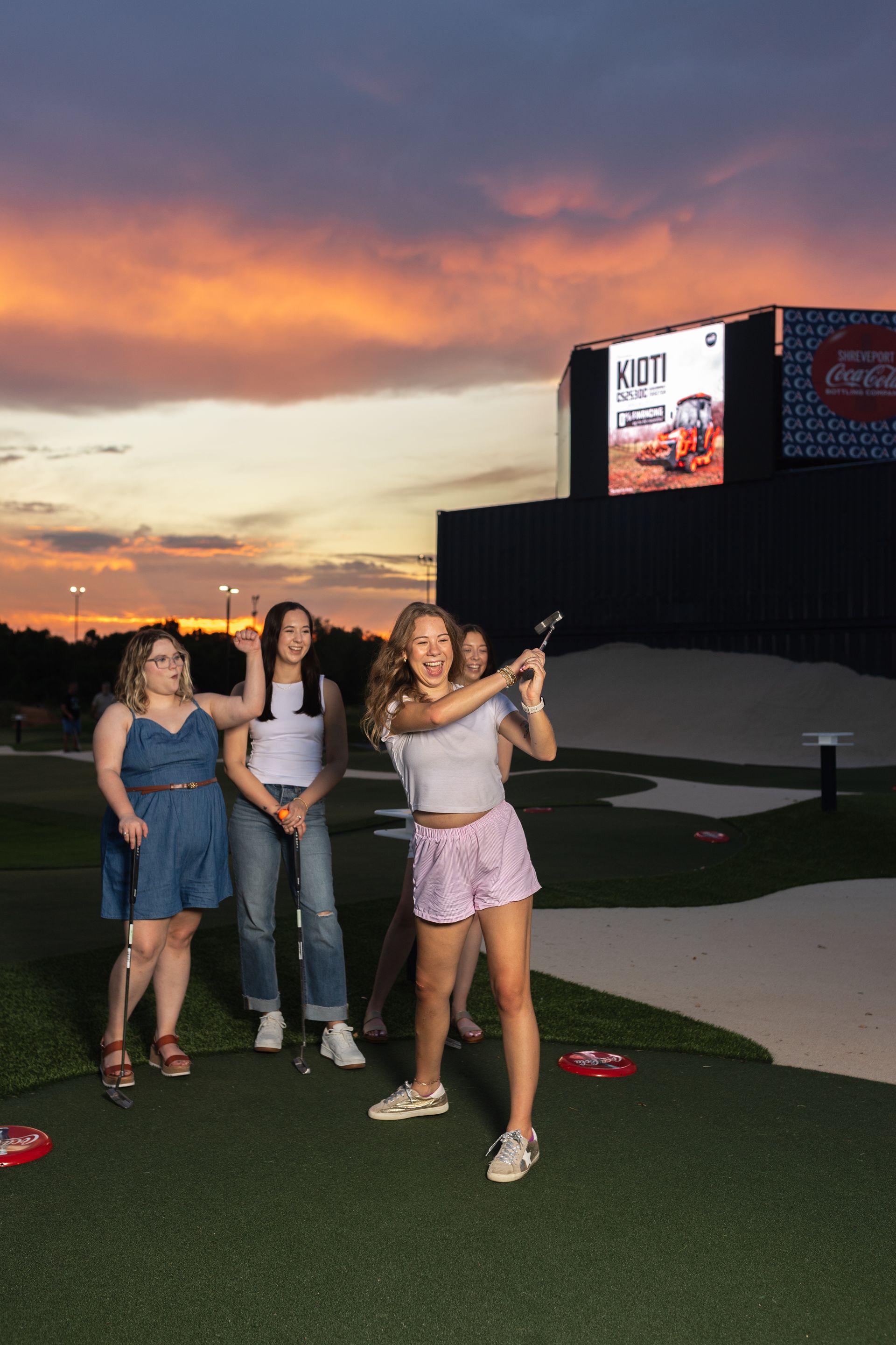 A group of people are standing on a golf course holding golf clubs in the air.