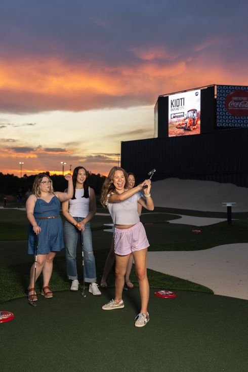 A group of people are standing on a golf course holding golf clubs in the air.