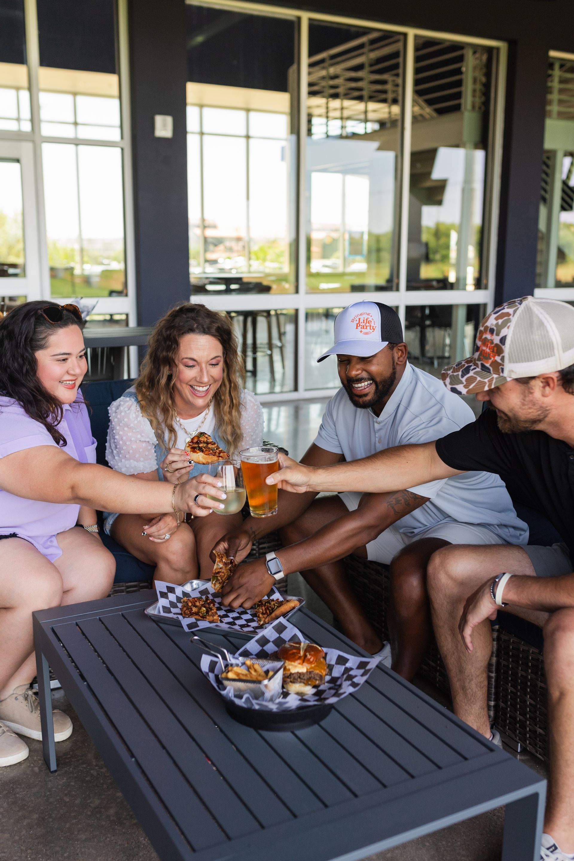 Friends toasting drinks around a patio table with a tray of appetizers in a casual outdoor setting