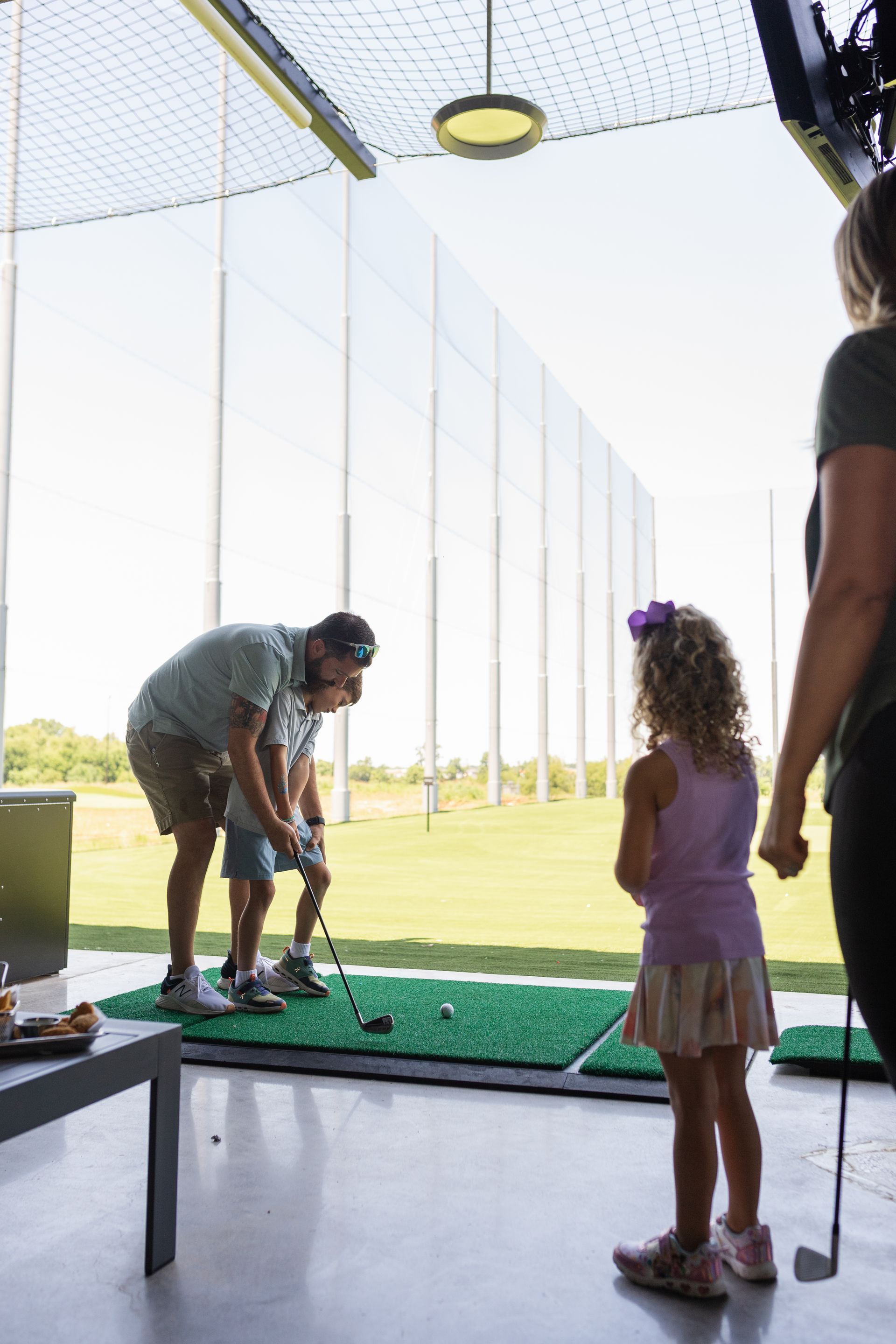 A man and a little girl are playing golf at a driving range.