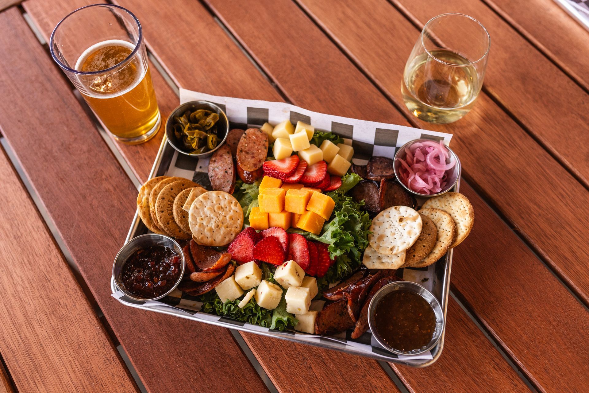 Outdoor table with a metal tray of assorted appetizers, bread, dips, fruit, and two drinks