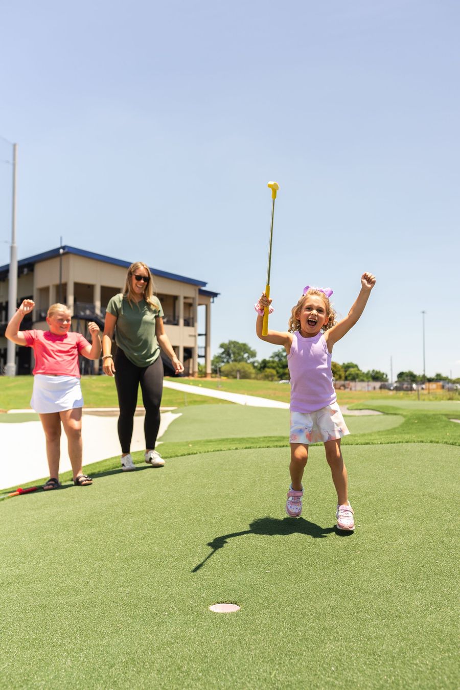 A little girl is jumping in the air while holding a golf club.