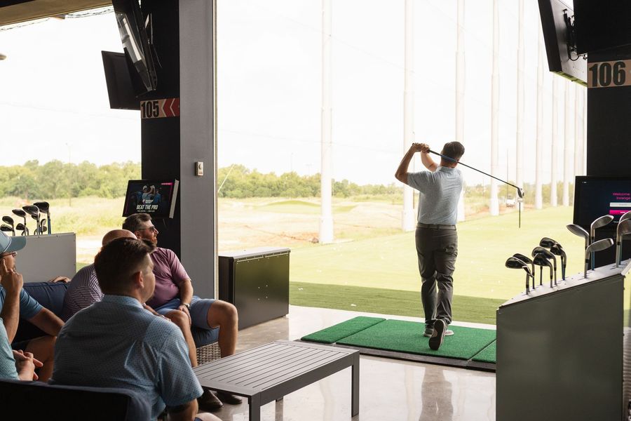 A group of people are sitting in a room watching a man swing a golf club.