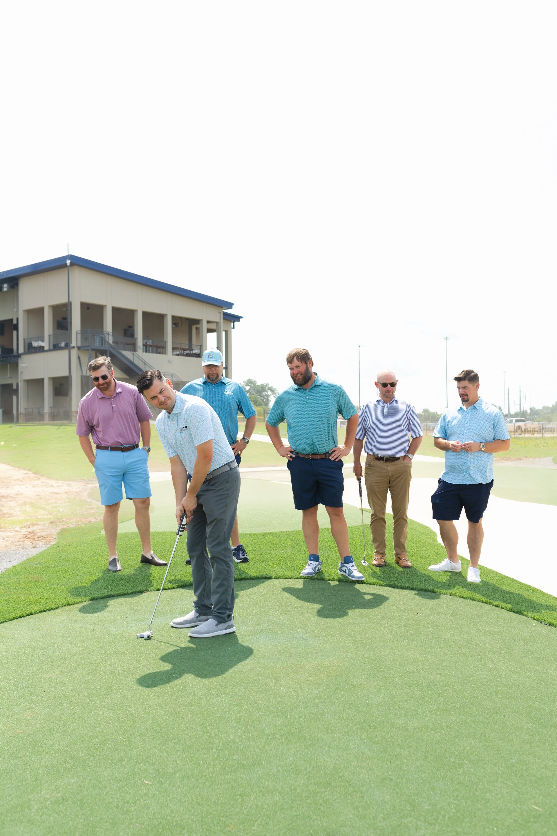Five people standing on a grassy field beside a building, outdoors on a sunny day.