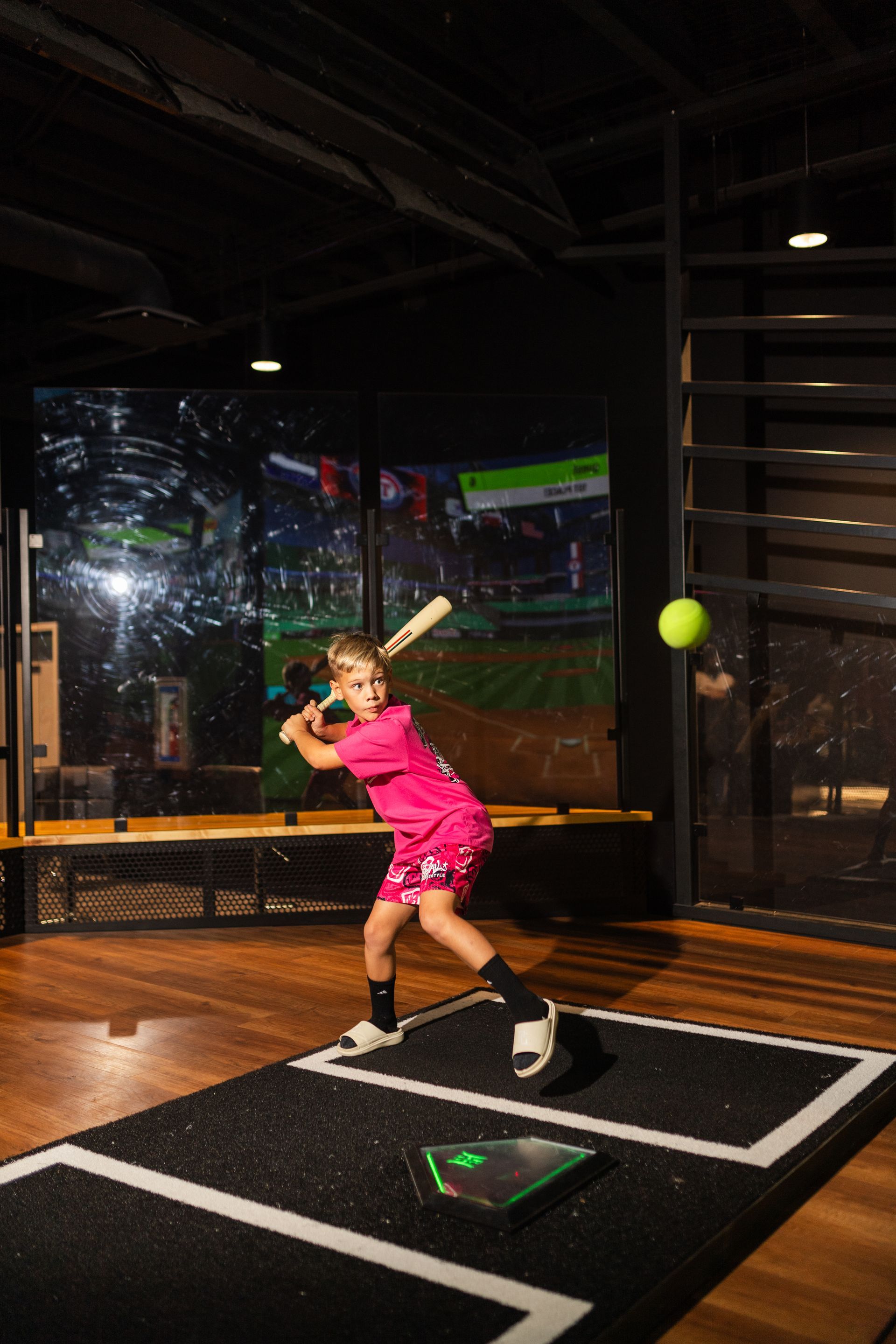 A kid is swinging a baseball bat at a virtual baseball game.