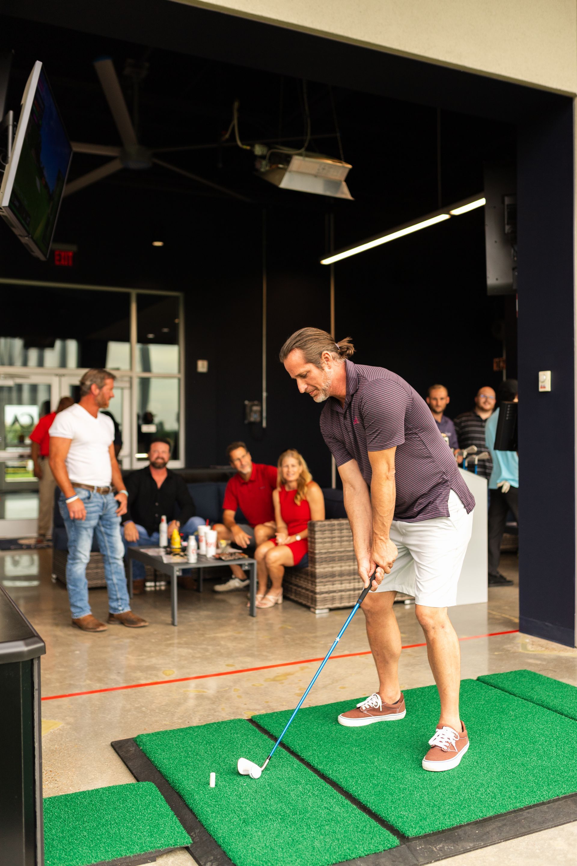 A man is swinging a golf club on a driving range while a group of people watch.