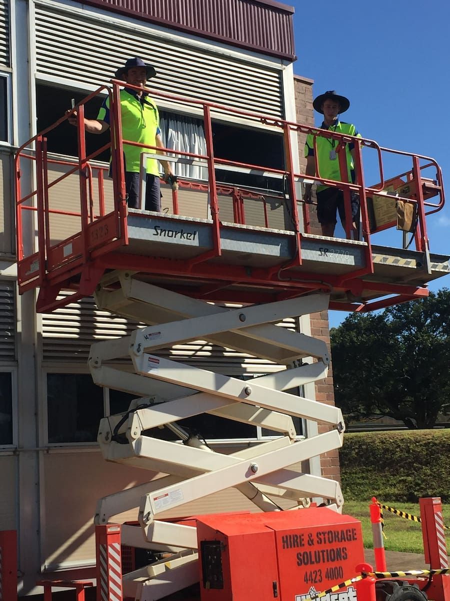 Two Men Are Working On A Scissor Lift In Front Of A Building — South Coast Glass In South Nowra, NSW