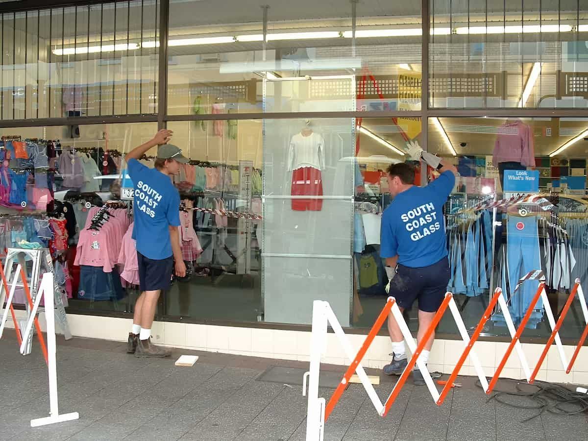 Two Men Wearing Blue South Coast Guard Shirts Are Cleaning A Store Window — South Coast Glass In Nowra, NSW