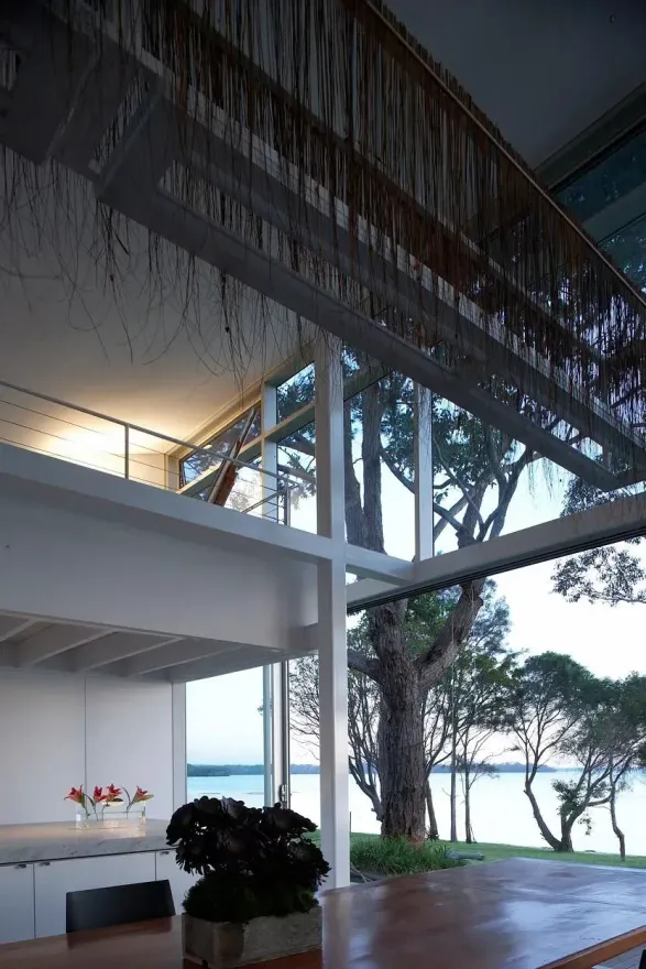 Interior view of a modern white house with large windows overlooking a lake, with a tree in the center — South Coast Glass In South Nowra, NSW