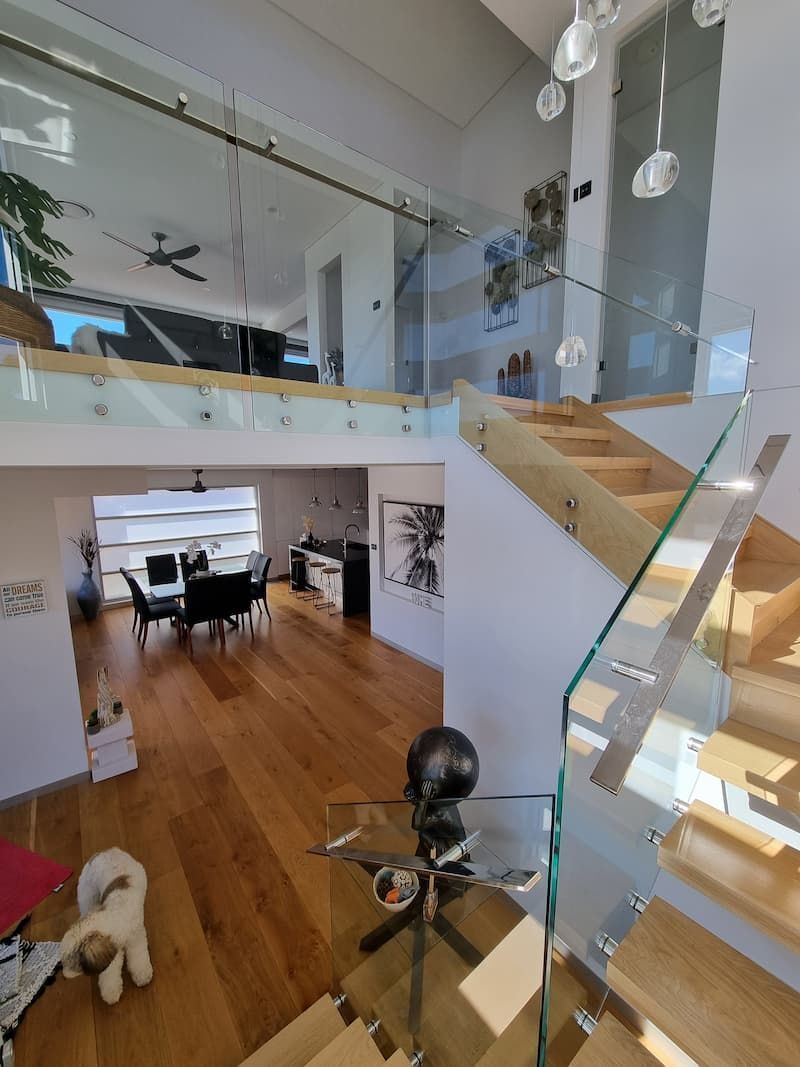 A Dog Is Sitting On The Floor In A Living Room Next To A Staircase — South Coast Glass In South Nowra, NSW