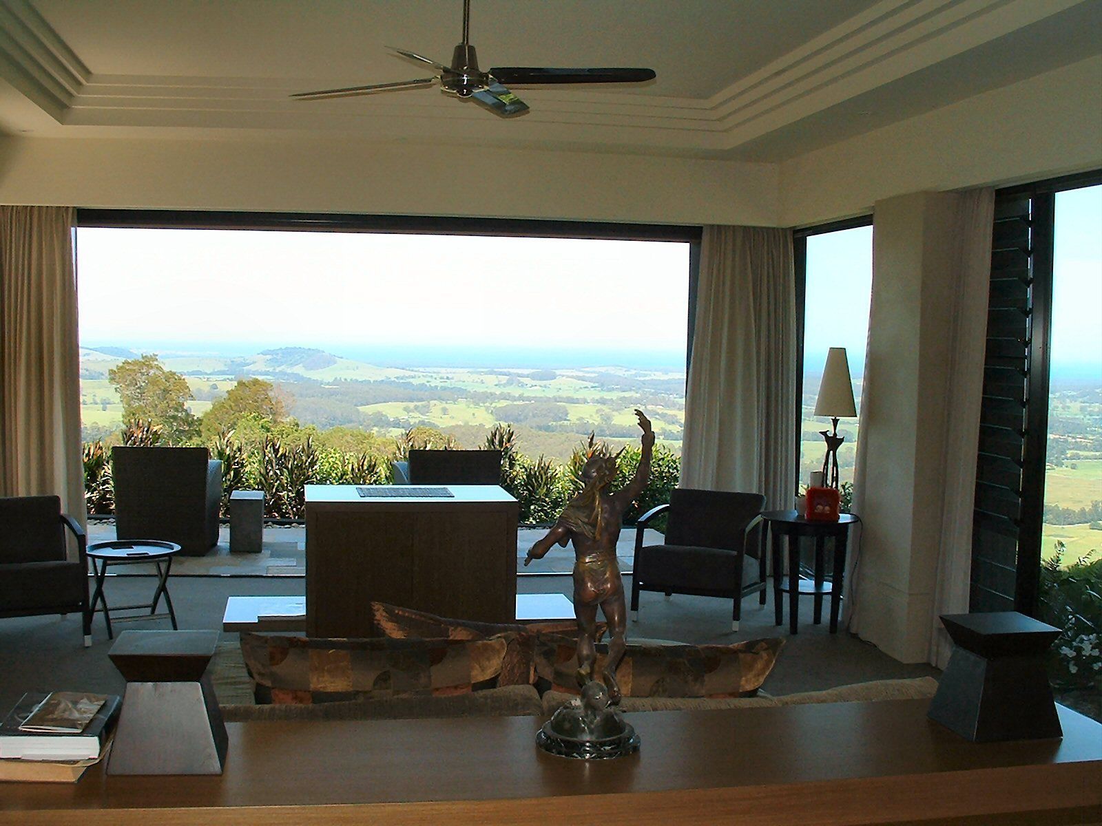 Living room with large windows overlooking a scenic landscape, furnished with chairs, a table, and a decorative sculpture — South Coast Glass In South Nowra, NSW
