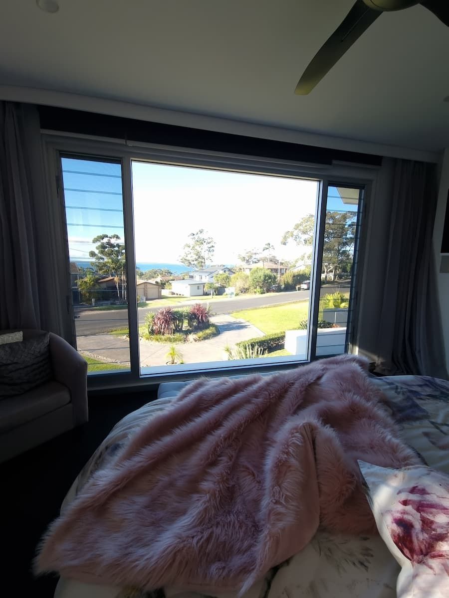 A Bedroom With A Large Window And A Bed With A Pink Blanket On It — South Coast Glass In South Nowra, NSW