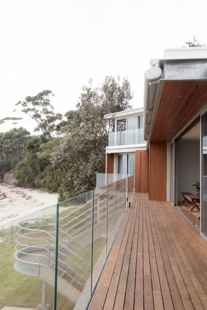 A Wooden Deck With A Glass Railing And A House In The Background — South Coast Glass In South Nowra, NSW
