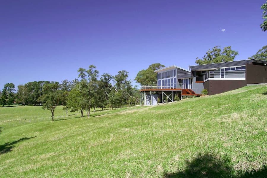 A Large House Is Sitting On Top Of A Grassy Hill Surrounded By Trees — South Coast Glass In South Nowra, NSW