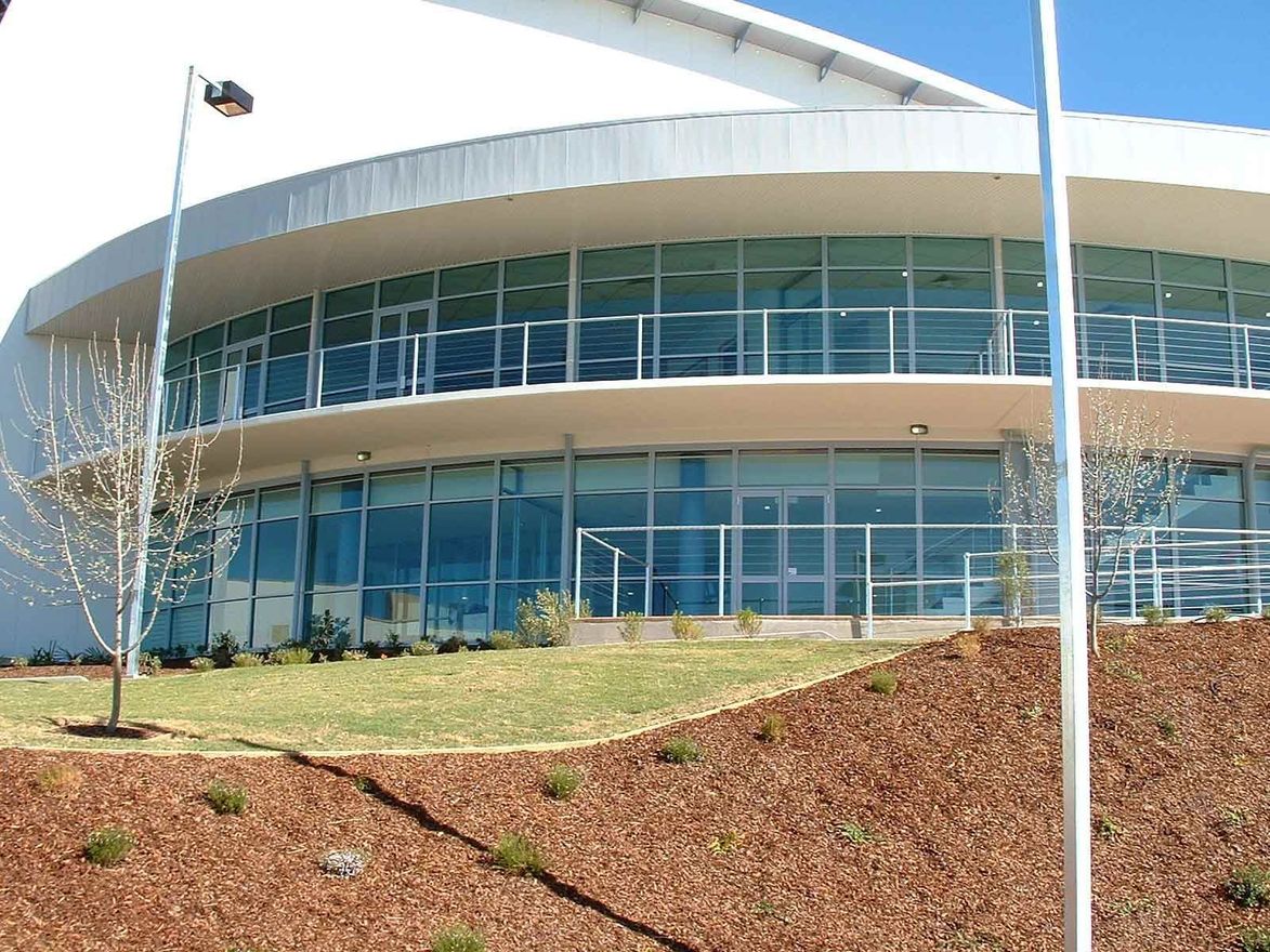 Modern building with curved glass windows, set on a brown, landscaped hill — South Coast Glass In South Nowra, NSW