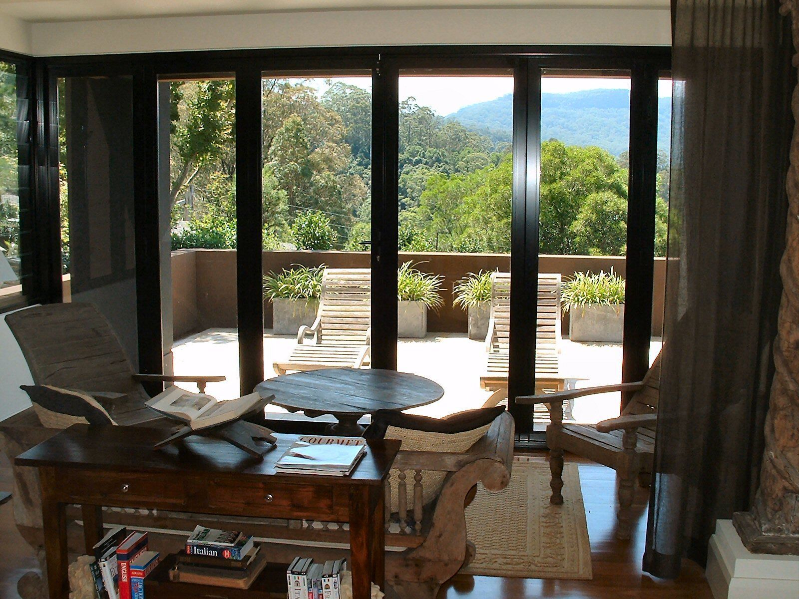 Room with large sliding doors open to a patio with lounge chairs, overlooking a tree-filled landscape — South Coast Glass In South Nowra, NSW