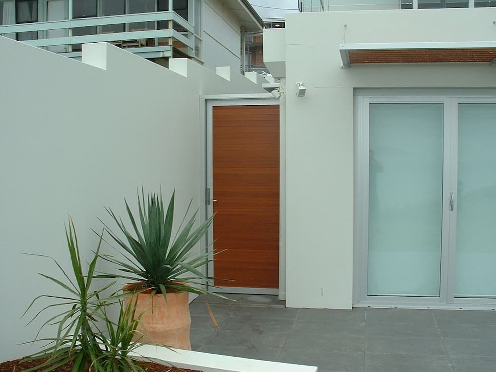 A White Building With A Wooden Door And A Potted Plant In Front Of It — South Coast Glass In South Nowra, NSW