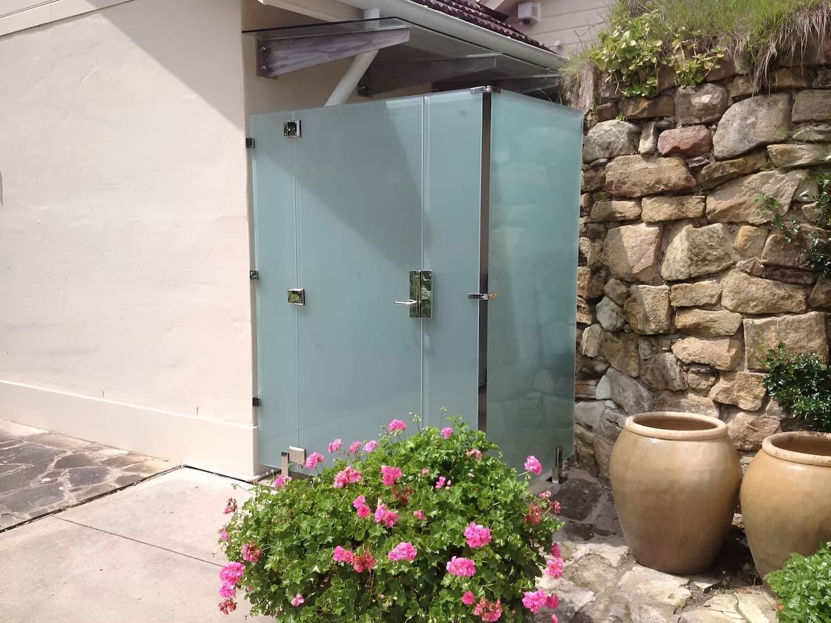 A Glass Shower Door Is Surrounded By Potted Plants And Flowers — South Coast Glass In Berry, NSW