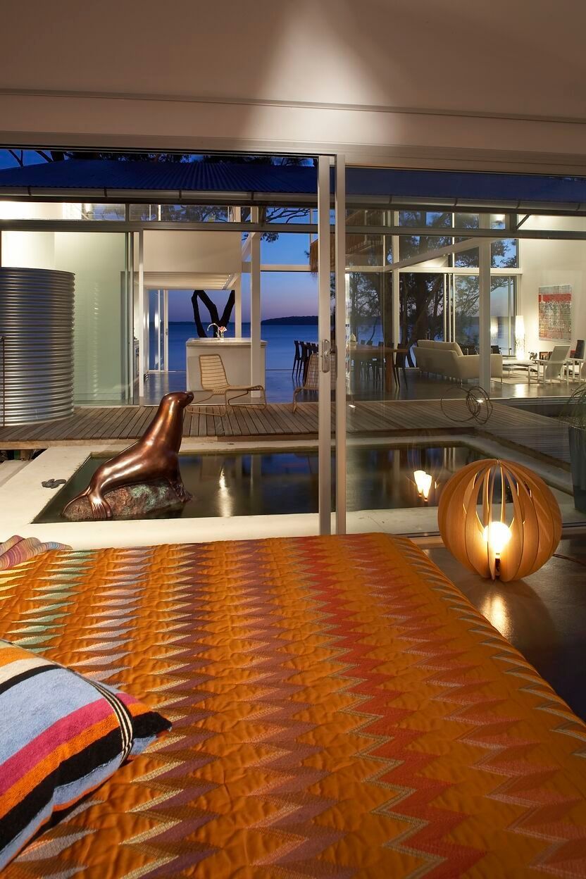 Bedroom with orange patterned bedspread and outdoor view through sliding glass doors, water feature with bronze sculpture — South Coast Glass In South Nowra, NSW